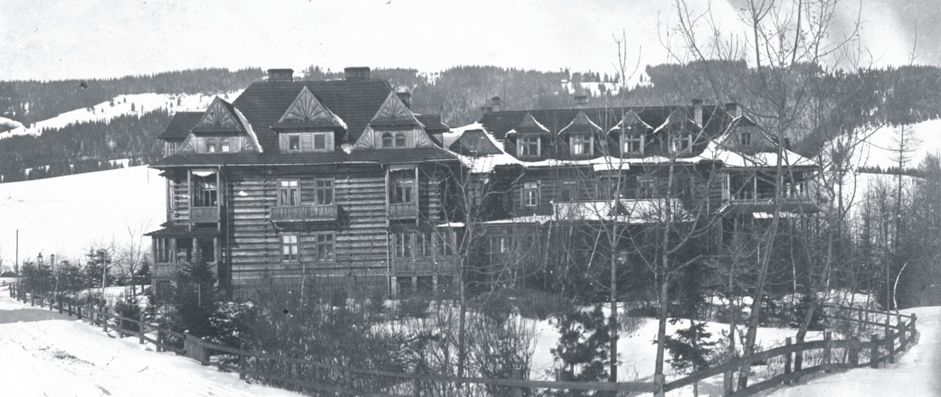 Na zdjęciu Pensjonat "Skoczyska", wybudowany w 1893 r. w stylu zakopiańskim. Budynek jest drewniany, ma trzy kondygnacje. Dach wykonany jest z drewnianych gątów. Wokół pensjonatu znajduje się drewniane ogrodzenie wykonane również z drewnianych żerdzi.