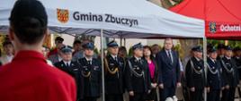 Goście uroczystości stoją pod namiotem z napisem "Gmina Zbuczyn".