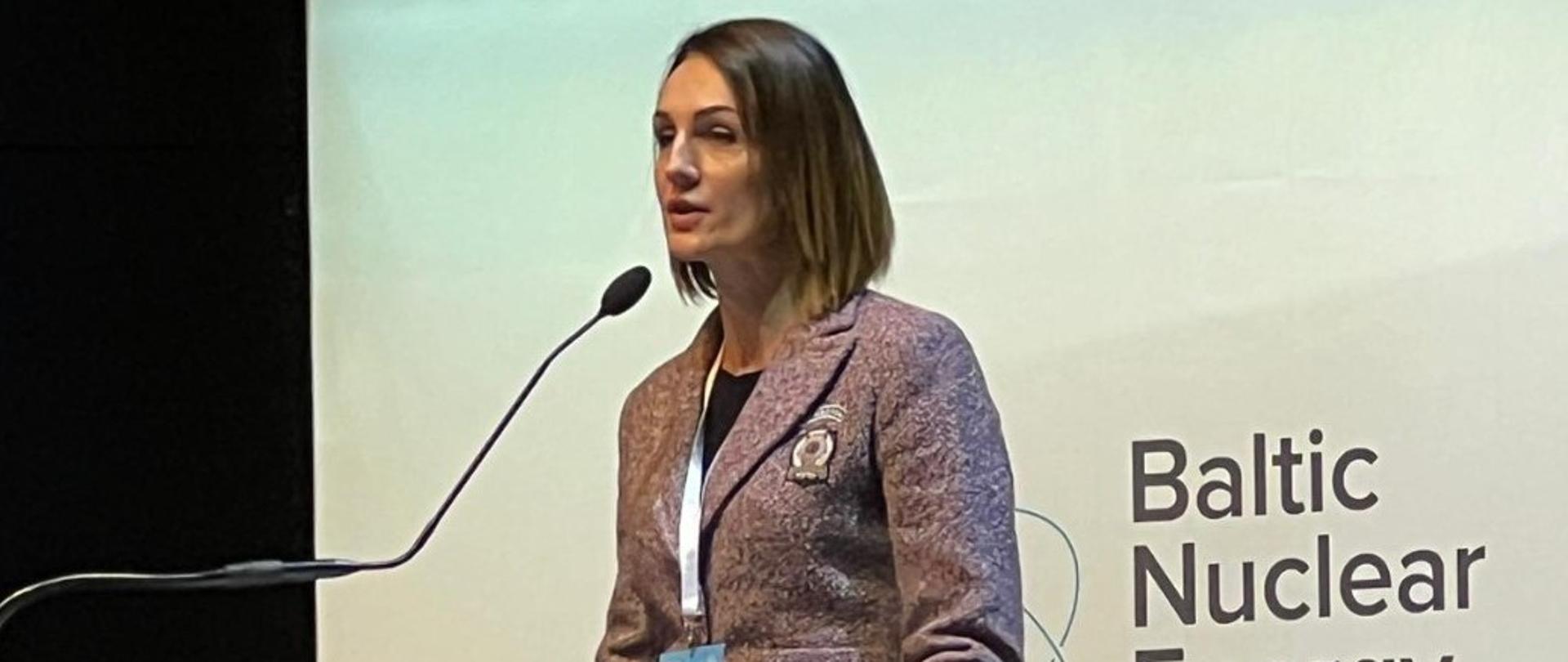 Kobieta (wojewoda) stoi przed mikrofonem, na tablicy za nią napis Baltic Nuclear