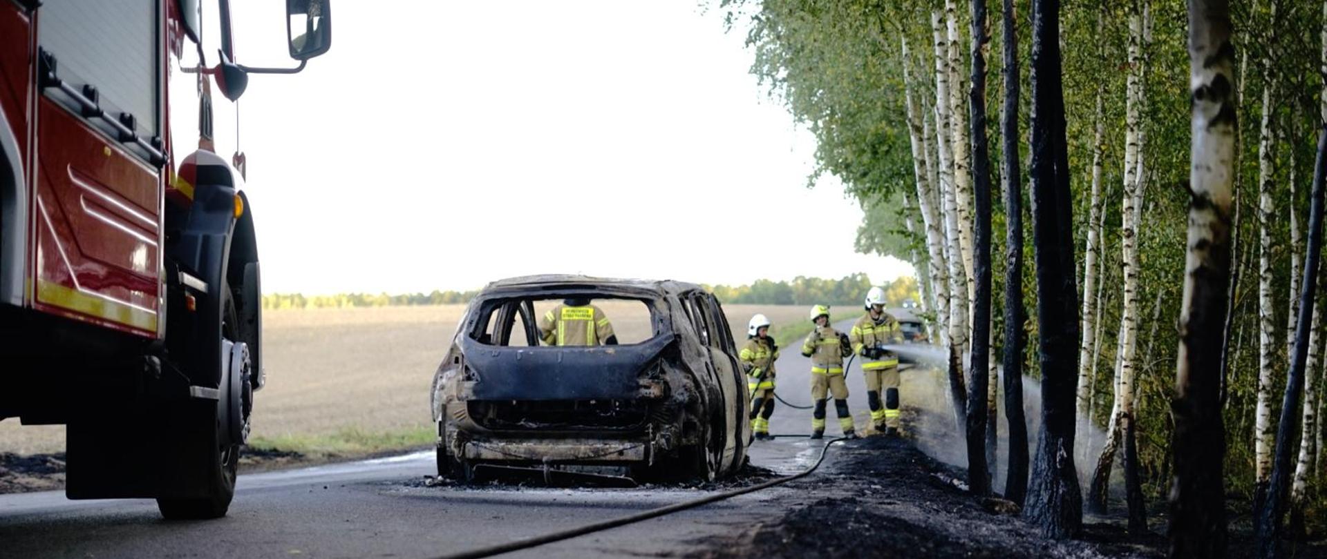 Na zdjęciu widoczny jest samochód osobowy po pożarze oraz ratownicy podczas przelewania pogorzeliska.
