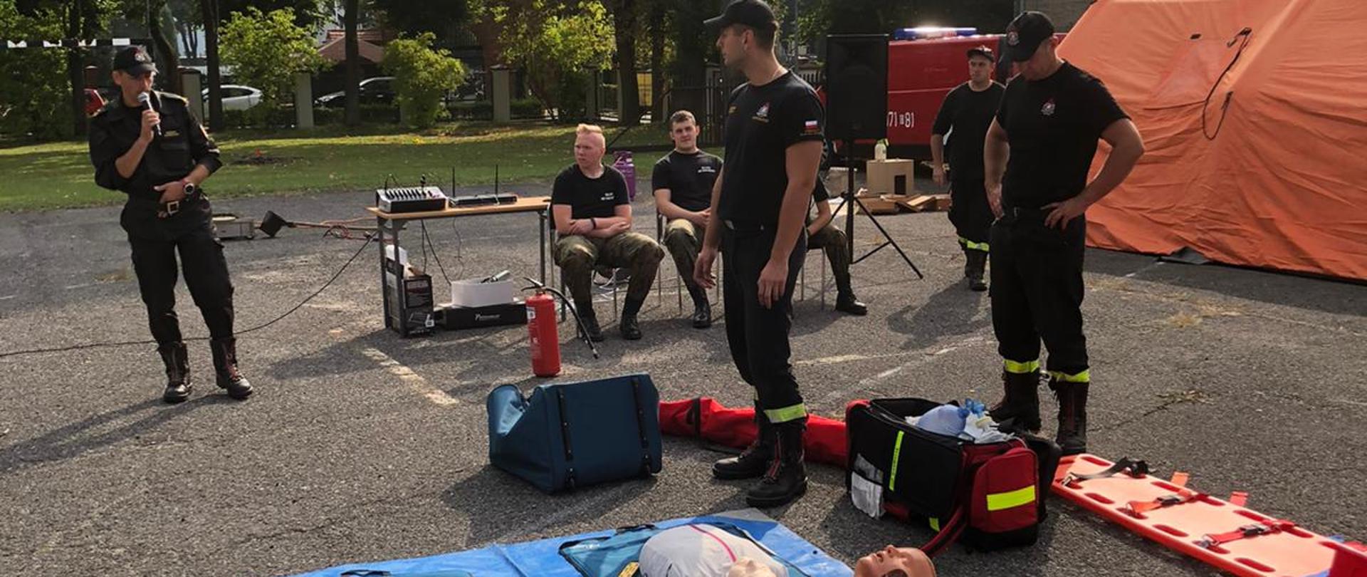 Na zdjęciu widać manekina oraz fantomy oraz sprzęt KPP ułożony na asfalcie. Z tył strażacy w ubranku koszarowym prezentują sprzęt.