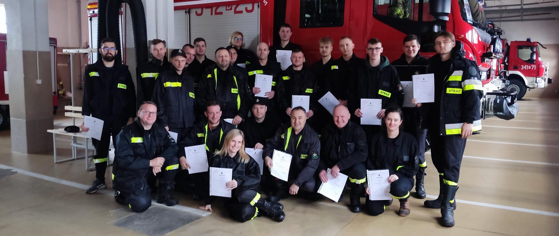 Druhowie OSP na garażu z zaświadczeniami na tel samochodu pożarniczego