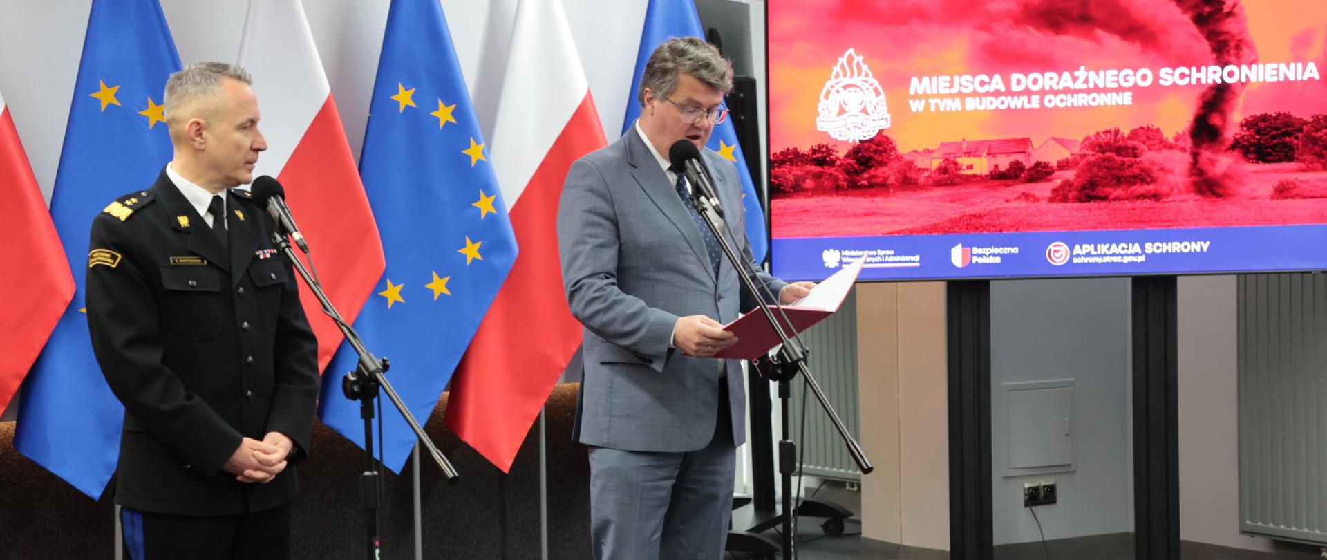 Wiceminister Maciej Wąsik oraz gen. brygadiera Andrzej Bartkowiak Komendant Główny PSP przemawiają przed mikrofonami podczas konferencji prasowej dot. inwentaryzacji budynków i obiektów budowlanych