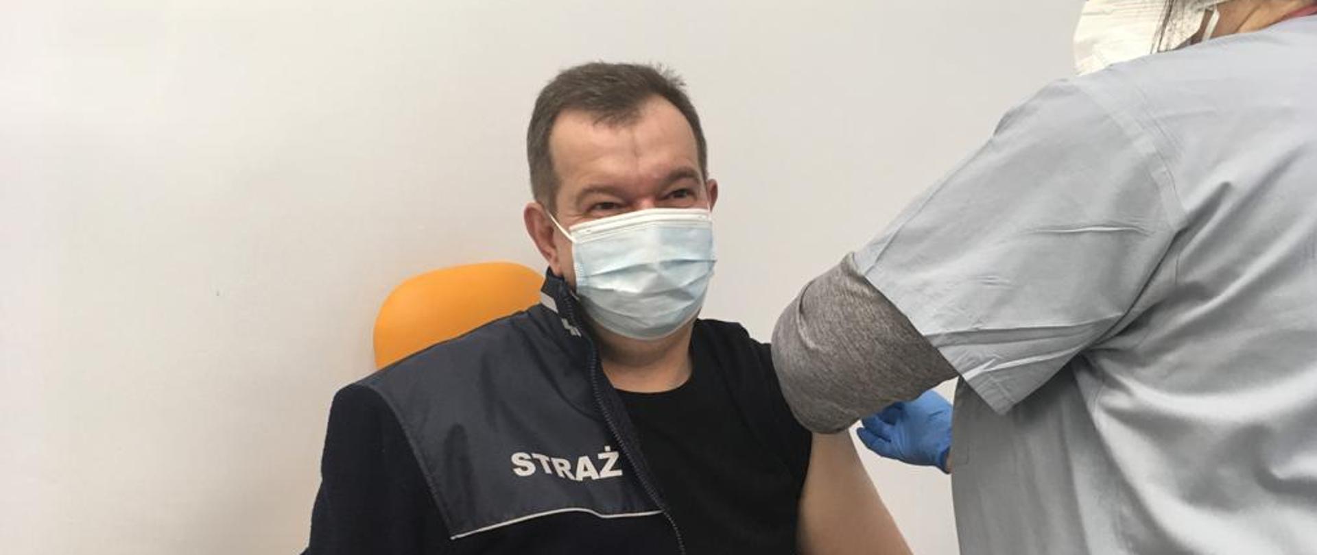 Zdjęcie przedstawia mężczyznę siedzącego na fotelu, który jest sczepiony przez pielęgniarkę.