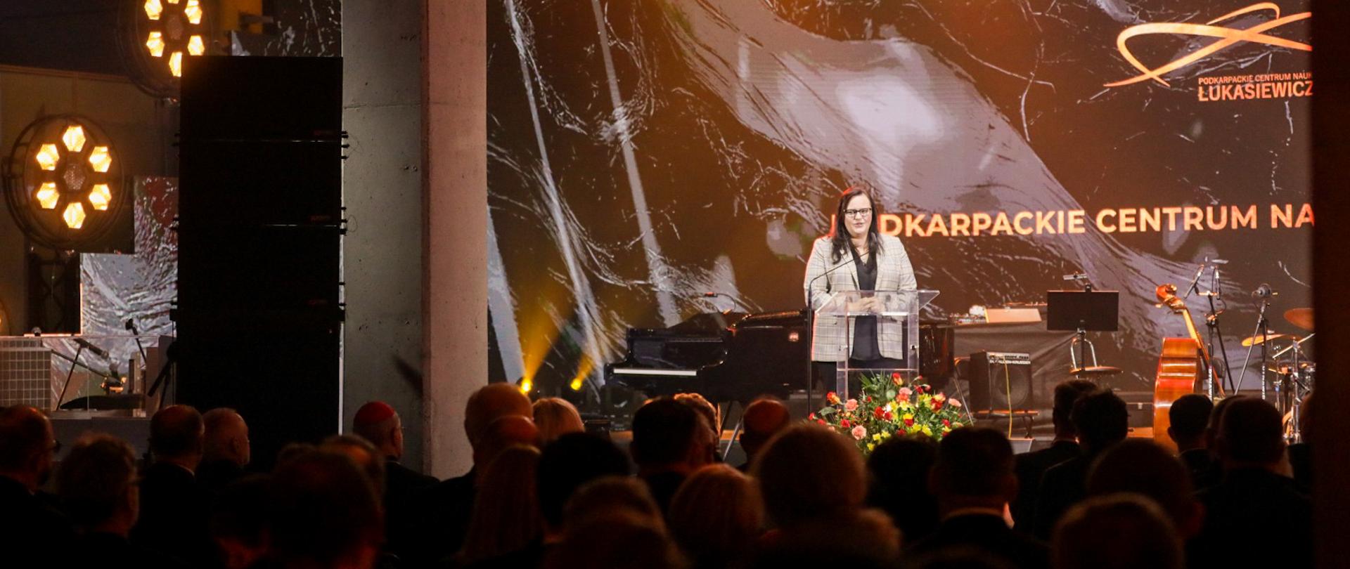 Wiceminister Małgorzata Jarosińska-Jedynak na scenie w mównicy. Przed nią publiczność