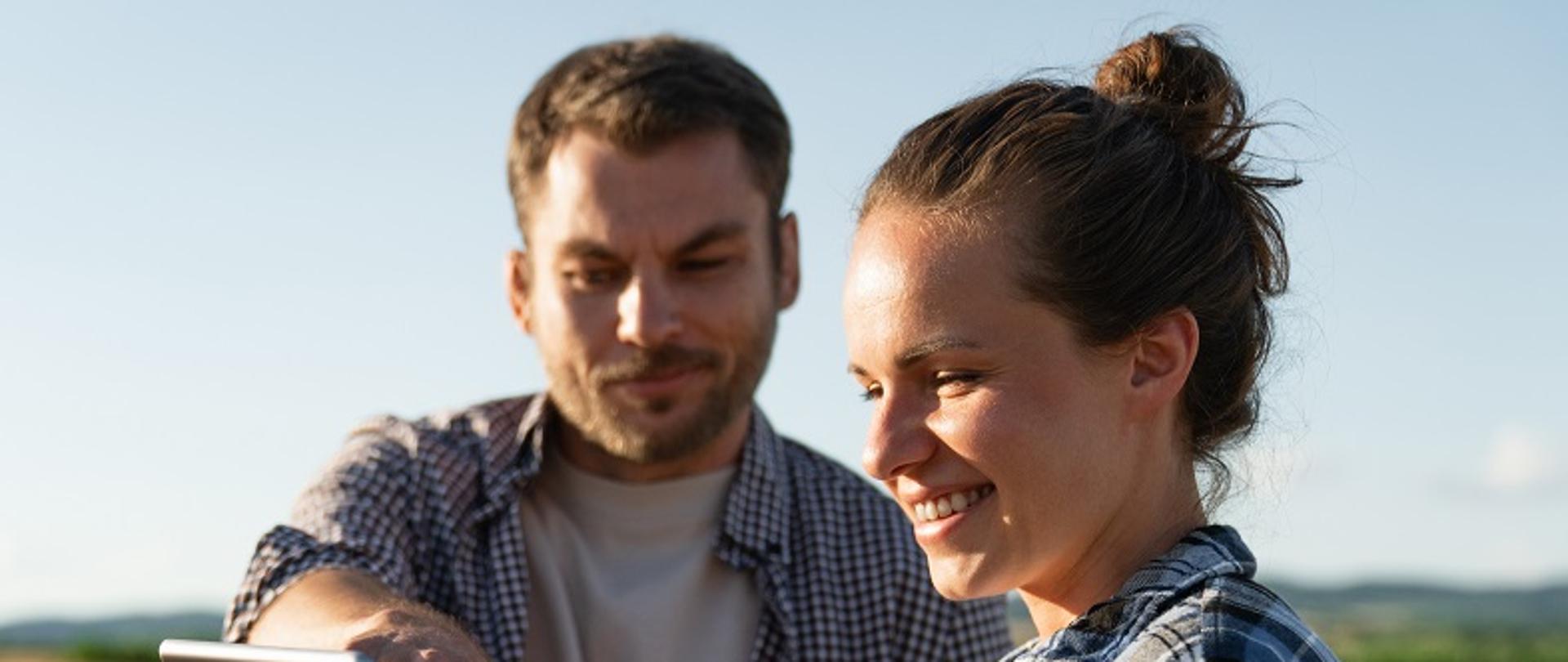 Para uśmiechniętych rolników na polu ogląda coś w tablecie