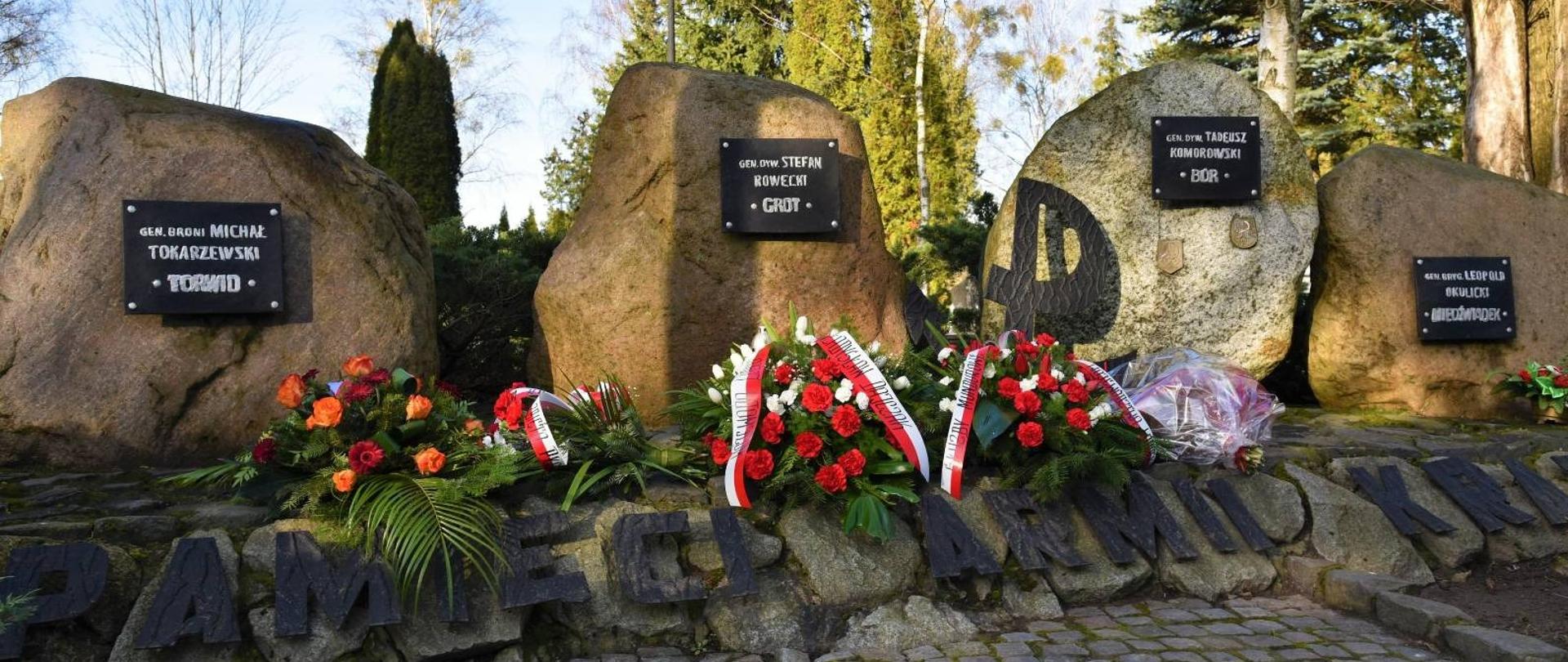 Pod Pomnikiem (4 obeliski z tablicami) leżą biało-czerwone wieńce i wiązanki kwiatów 