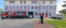 Strażacy zgromadzeni na placu przed jednostką salutują przed podniesioną flagą
