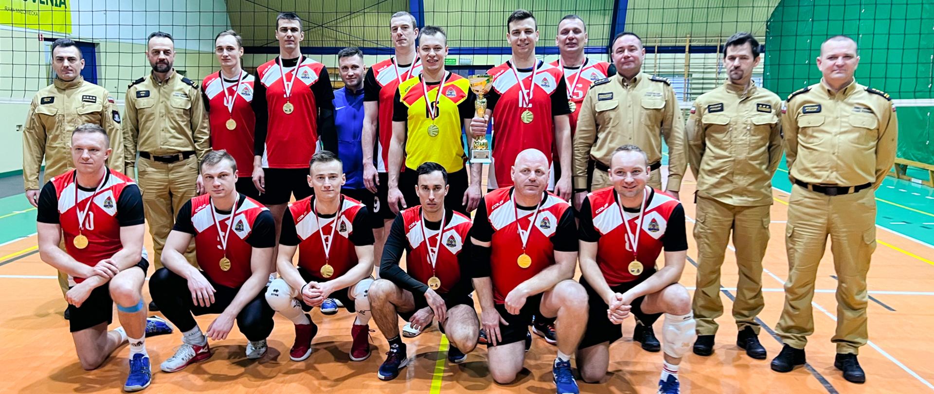 strażacy - zawodnicy zwycięskiej drużyny oraz komendanci pozują do zdjęcia w hali sportowej