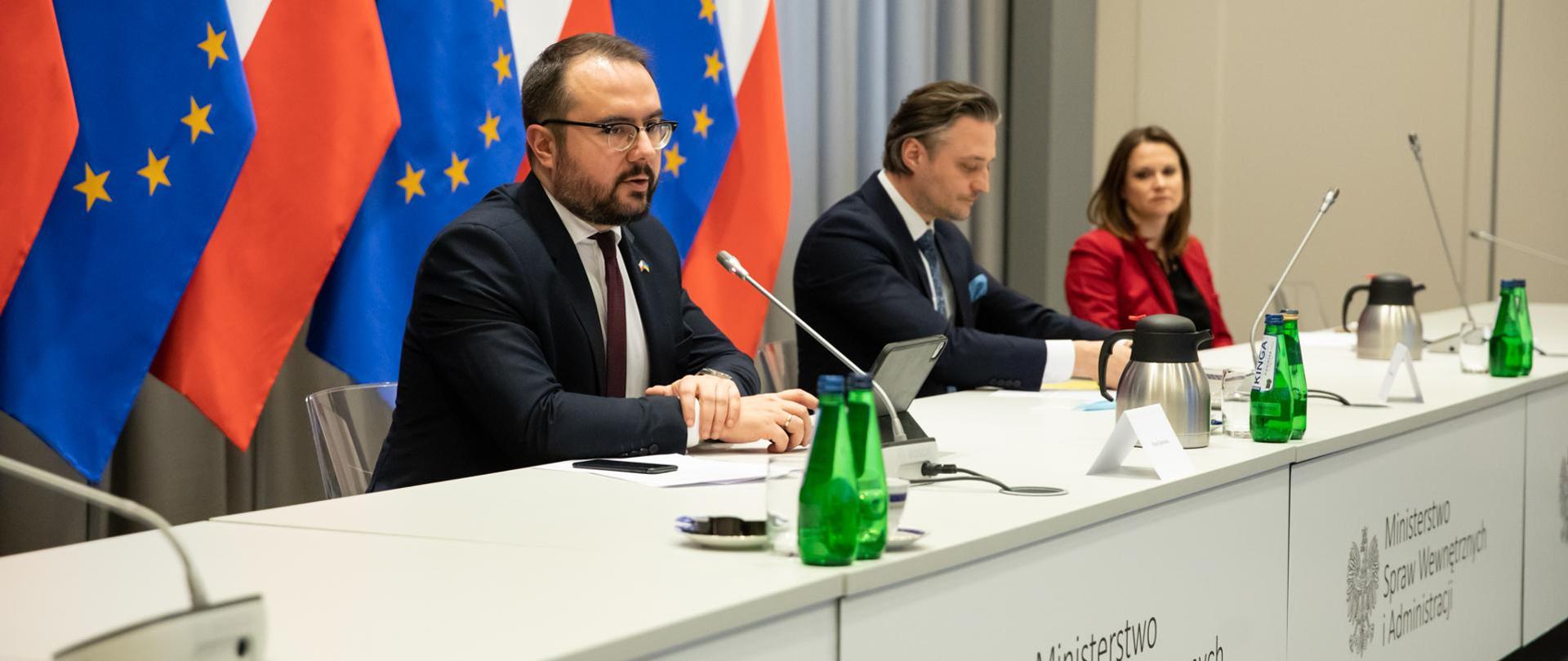Minister Jabłoński siedząc przy stole mówi do mikrofonu