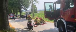 Strażacy udzielają kwalifikowanej pierwszej pomocy rannemu motorowerzyście. 