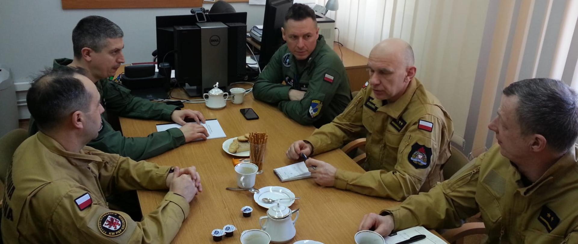 Zdjęcie przedstawia biuro a w nim stół przy którym prowadzone są rozmowy przedstawicieli z wojska oraz ze straży.