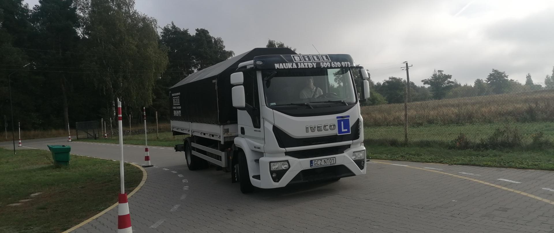 Zdjęcie przedstawia samochód ciężarowy nauki jazdy na placu manewrowym. Za kierownicą strażak ratownik z Ochotniczej Straży Pożarnej.