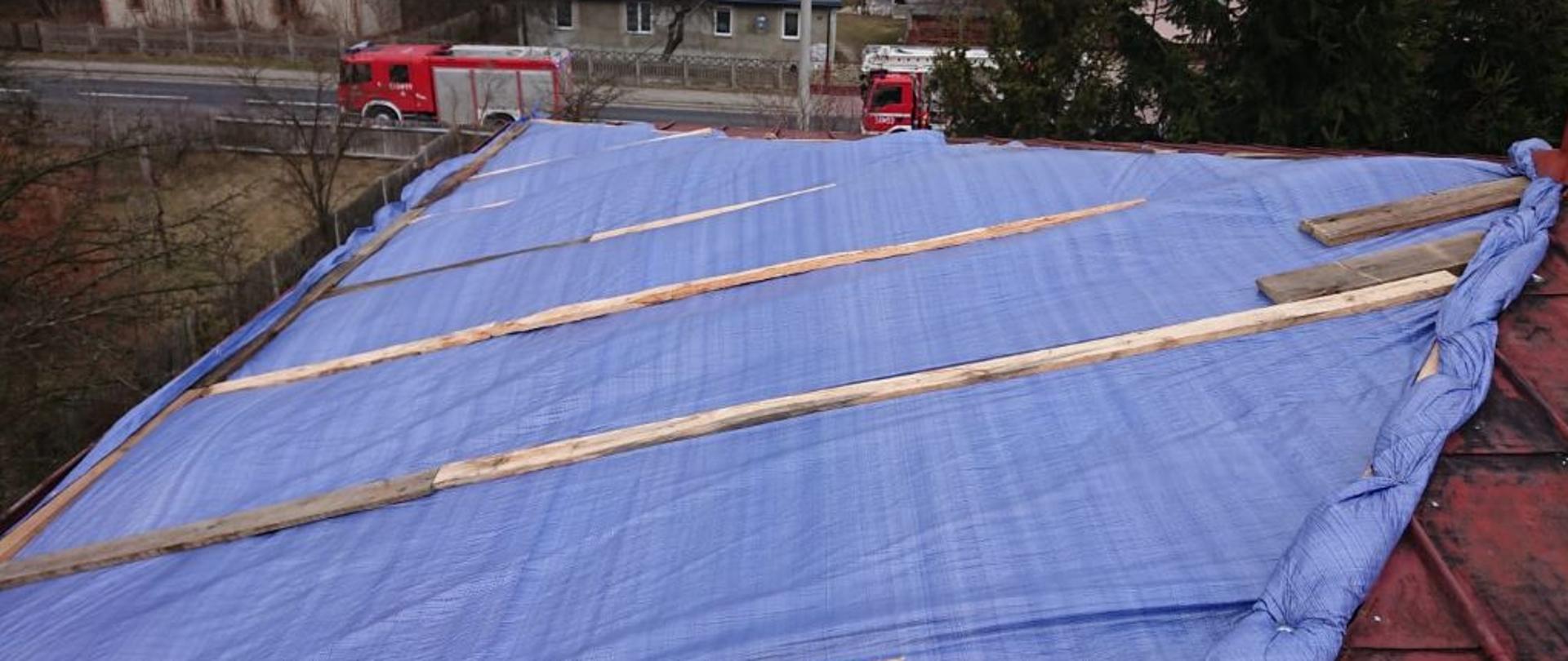 Na pierwszym palnie dach budynku mieszkalnego, z uszkodzonym pokryciem dachowym, powstała dziura została zabezpieczona plandeką oraz deskami