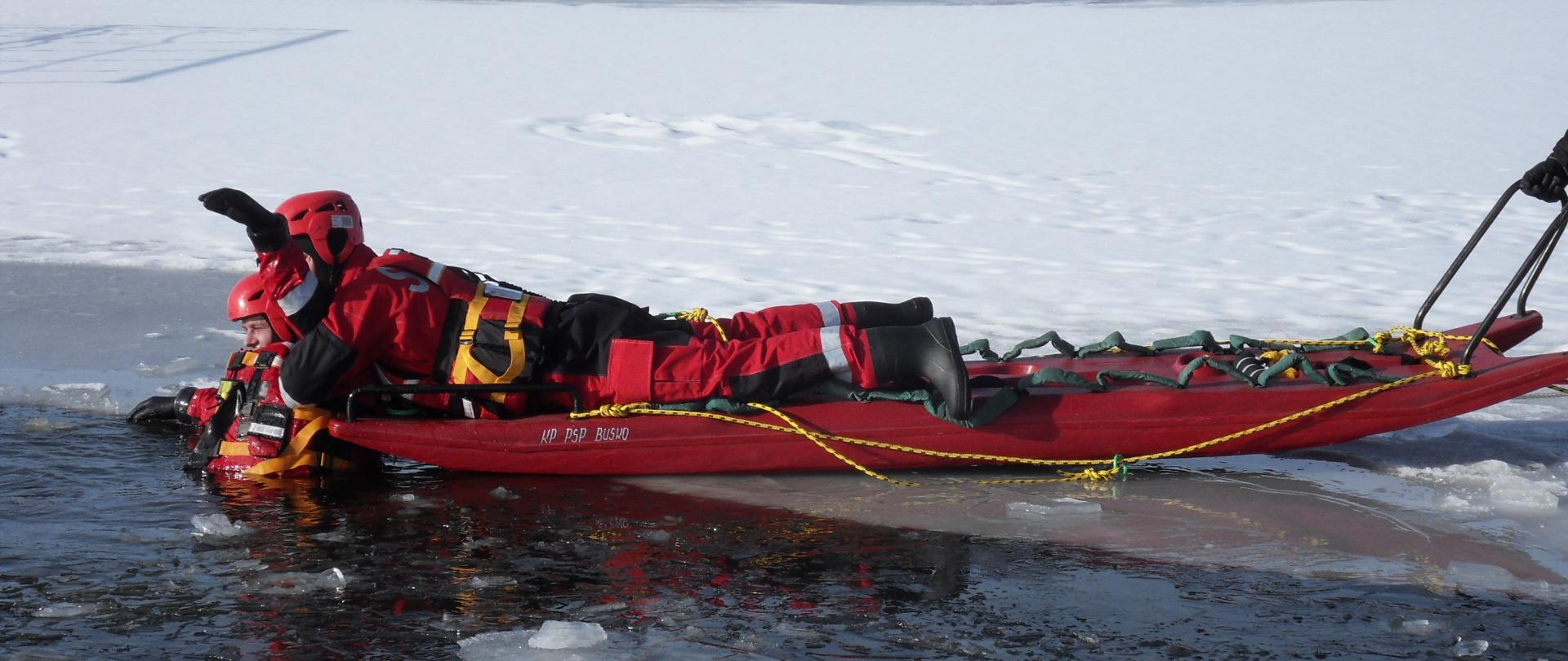 Strażak leżący na saniach lodowych,wyciągający osobę z przerębli na zbiorniku wodnym