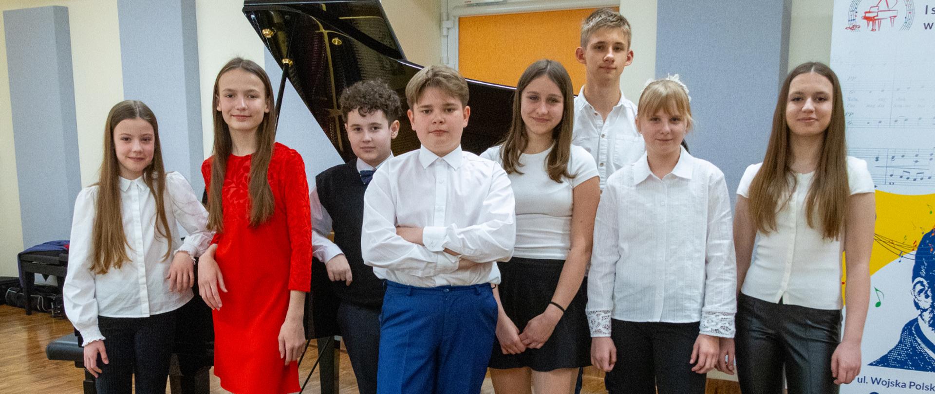 Grupa kilku uczniów stoi przy fortepianie.