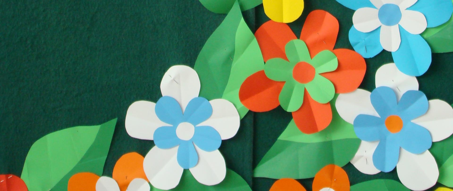 Zdjęcie przedstawia kolorowe kwiaty z papieru na zielonym tle