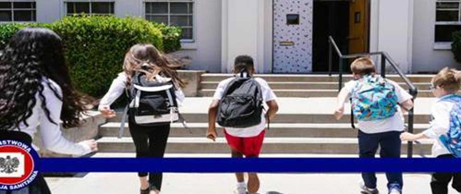 Zdjęcie przedstawia piecioro dzieci z plecakami szkolnymi wchodzących na schody przed drzwiami szkoly