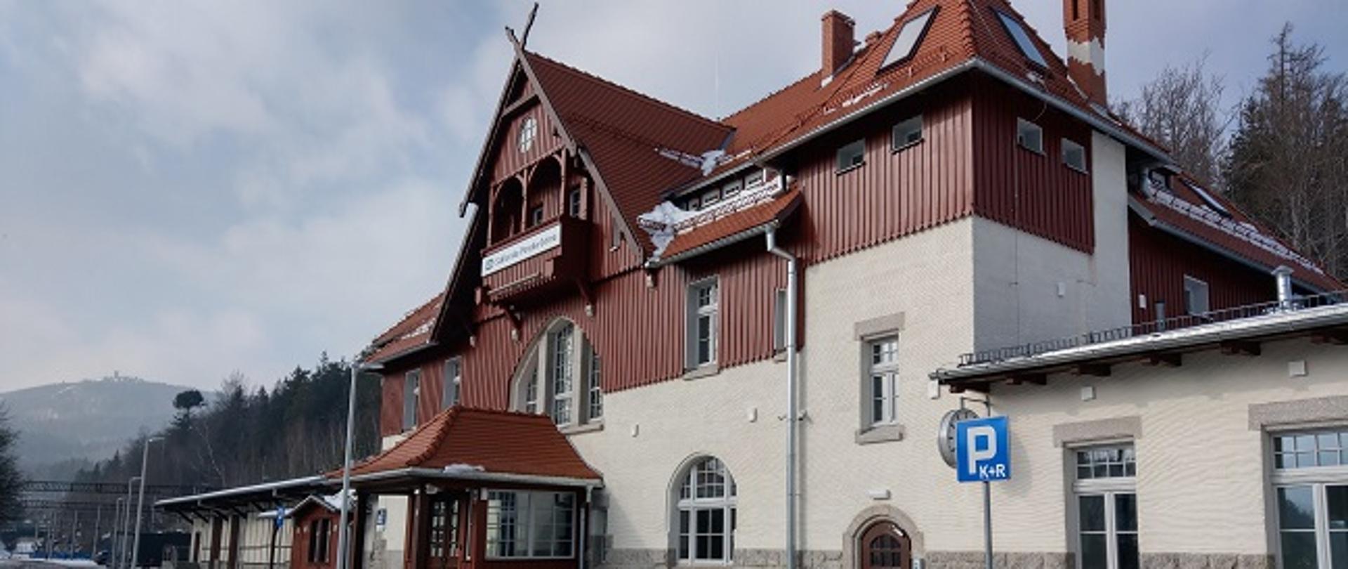 Zdjęcie przedstawia odnowiony dworzec w Szklarskiej Porębie. Budynek ma jasną elewację z drewnianymi elementami.