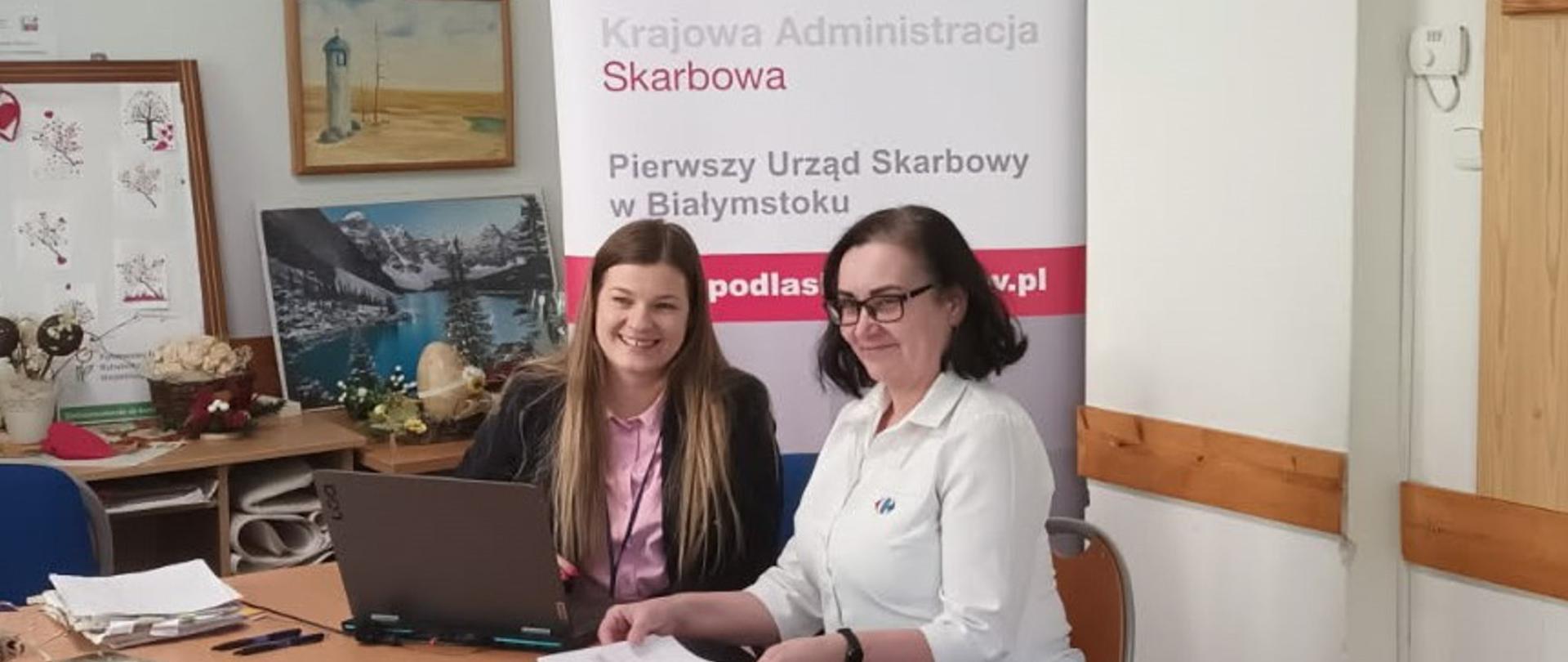 Pracownik I US w Białymstoku wspiera osobę z niepełnosprawnością w rozliczeniu PIT, pracownik przy laptopie, podatnik trzyma dokumenty, siedzą przy biurku