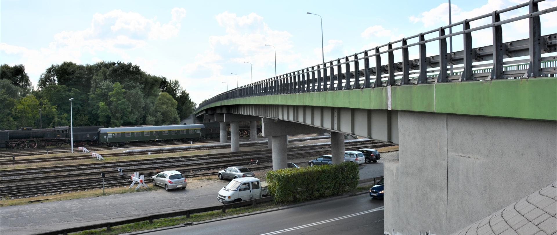 wiadukt w m. Wolsztyn widok z boku, w tle widoczne tory, pociąg, na pierwszym planie droga