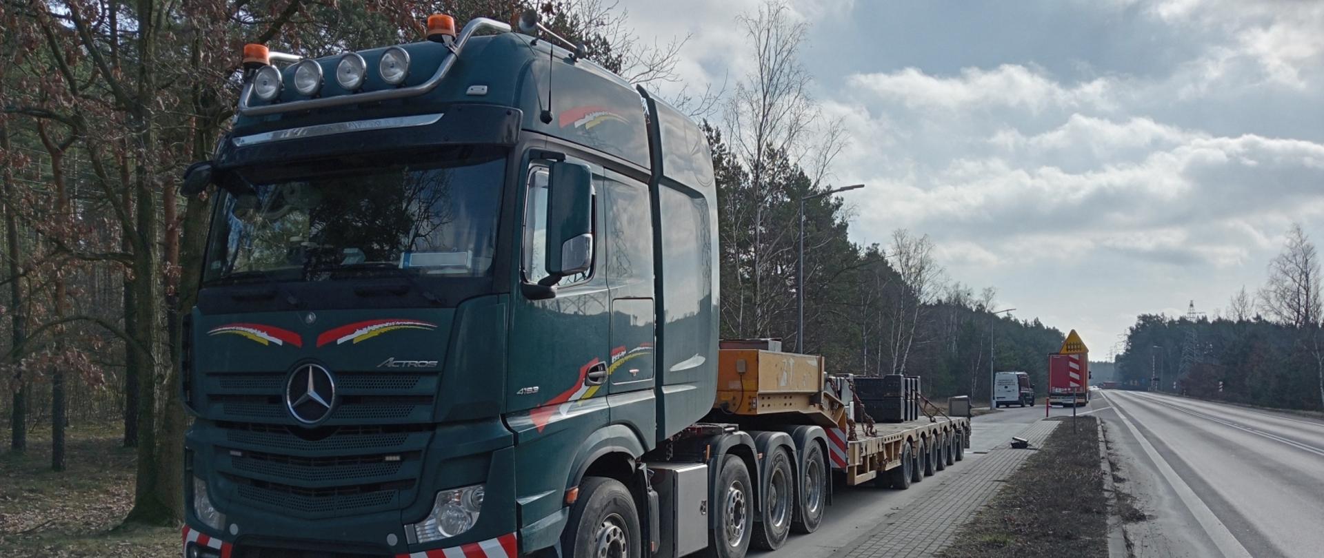 Na pierwszym planie pojazd ciężarowy podczas kontrolii, za nim w tle widoczny pojazd Inspekcji Transportu Drogowego.