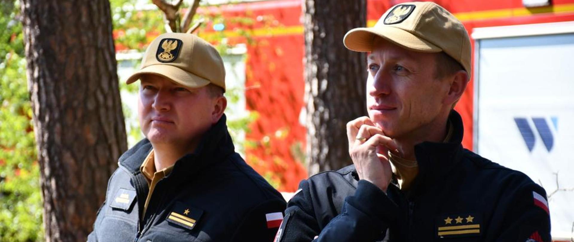 dwóch strażaków w czapeczkach stoi w lesie