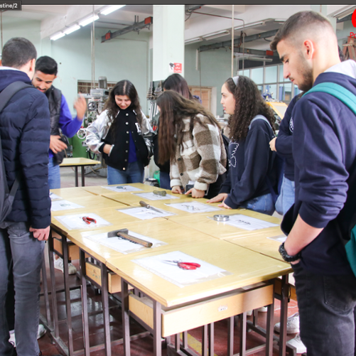 Grupa młodzieży stoi wokół stołu, na którym rozłożone są narzędzia i słucha nauczyciela