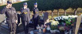 Widok z boku. Trzech strażaków PSP salutuje na cmentarzu przed grobem.