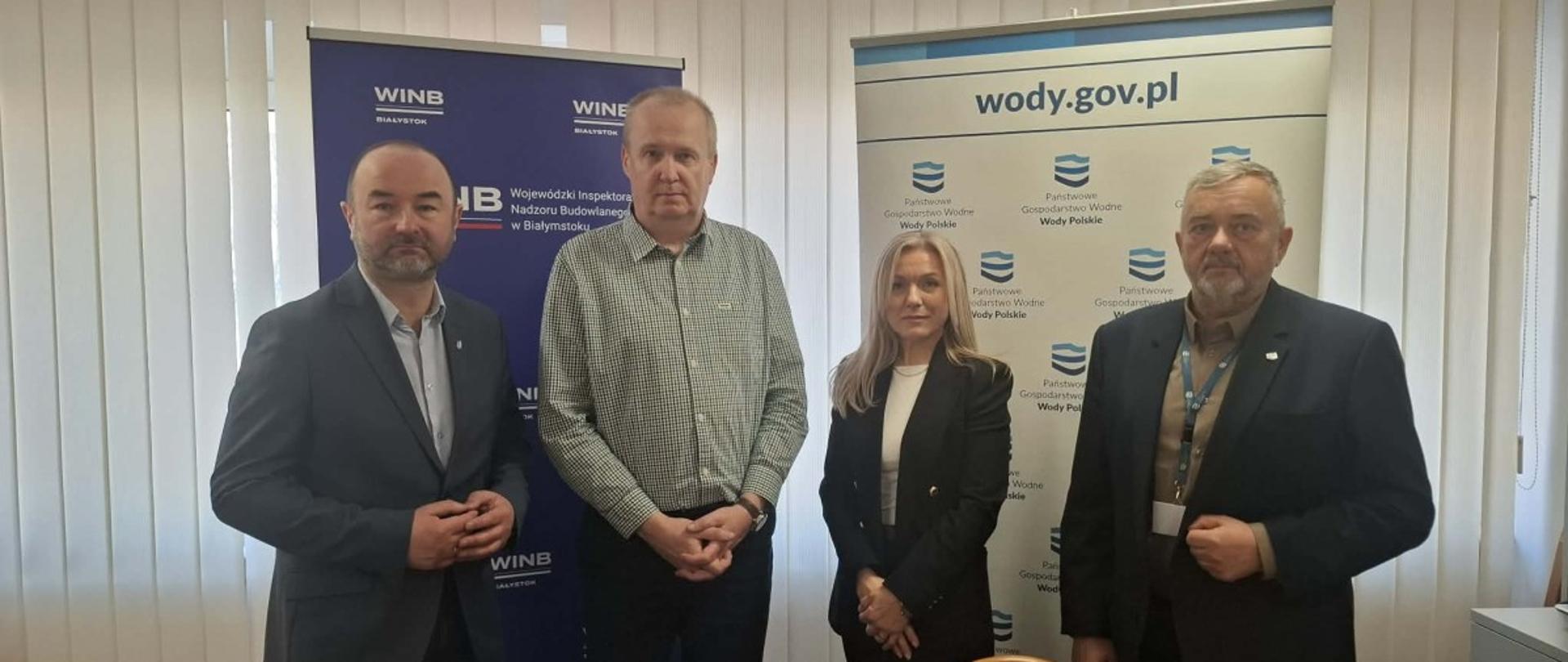 Grupa składająca się z trzech mężczyzn i jednej kobiety stoi przy stole, angażując się w dyskusję. 