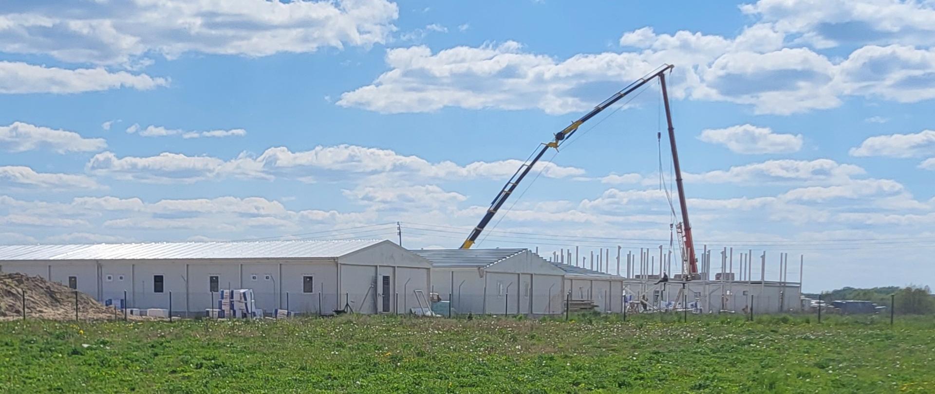 Powstające budynki , długie, parterowe na środku łąki 