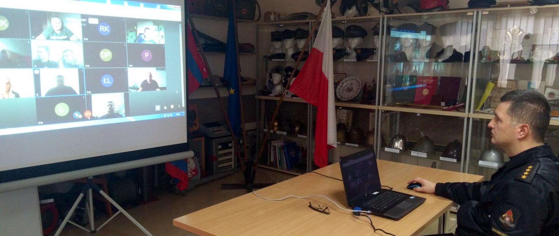 Na zdjęciu oficer PSP przed komputerem, z lewej strony strażacy osp na rzutniku multimedialnym.