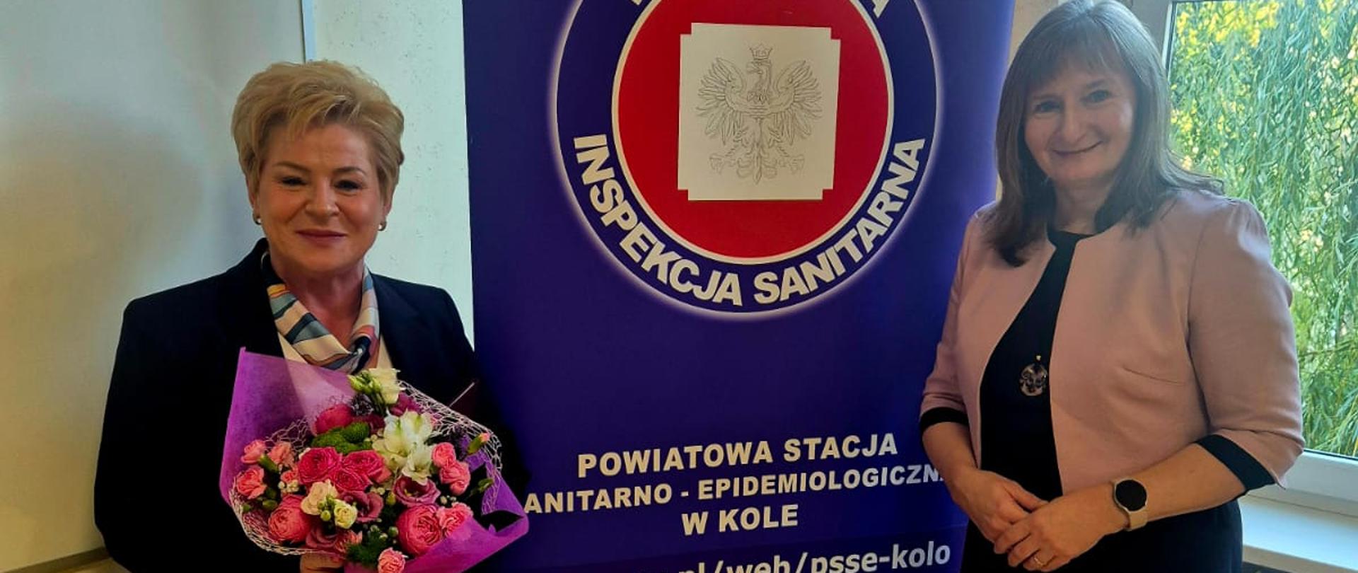 dwie kobiety stojące na tle baneru inspekcji sanitarnej w Kole