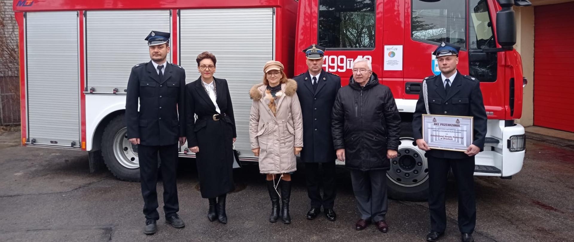 Na tle bojowego samochodu pożarniczego stoją członkowie OSP w Brodach w mundurach galowych wraz zaproszonymi gośćmi