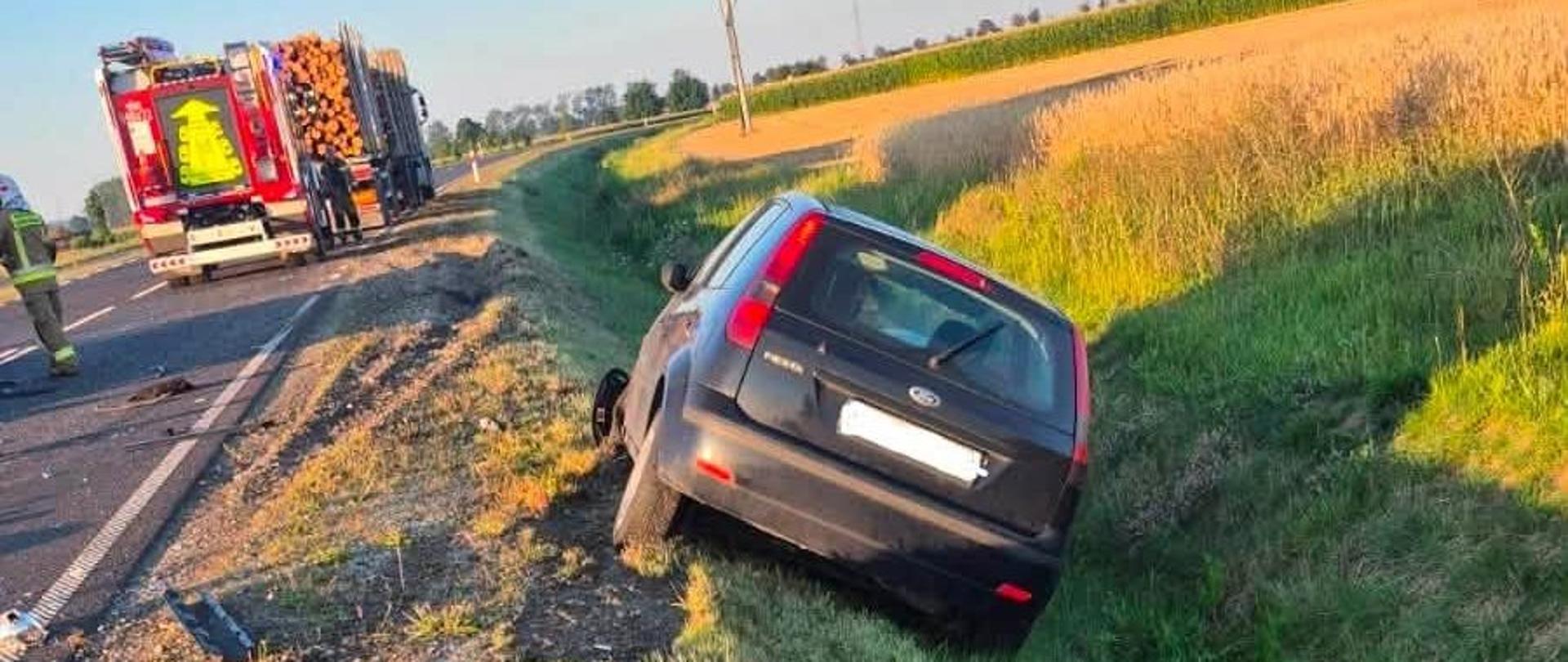 Ciemny samochód w rowie, za nim pojazd straży pożarnej