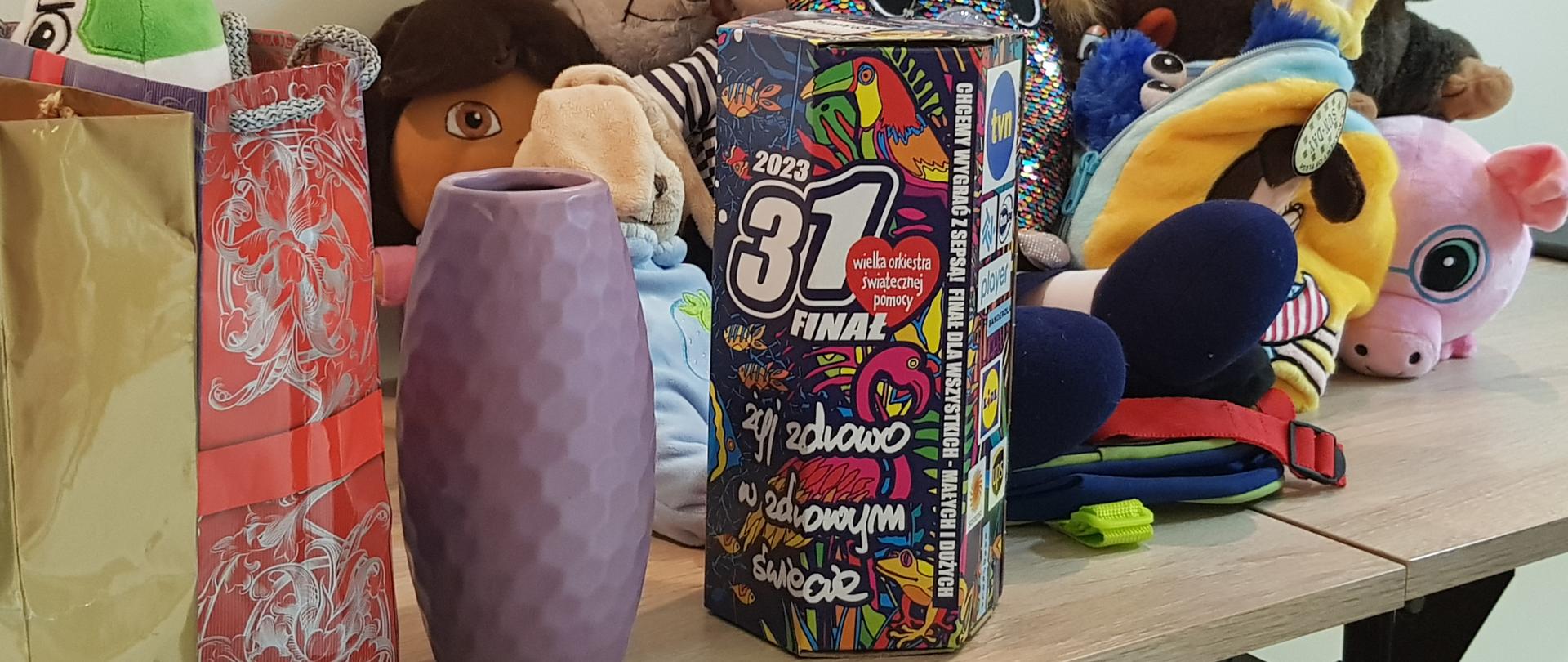 zdjęcie przedstawia pluszaki i fanty przeznaczone na licytację oraz puszkę z logiem Wielkiej Orkiestry Świątecznej Pomocy. 