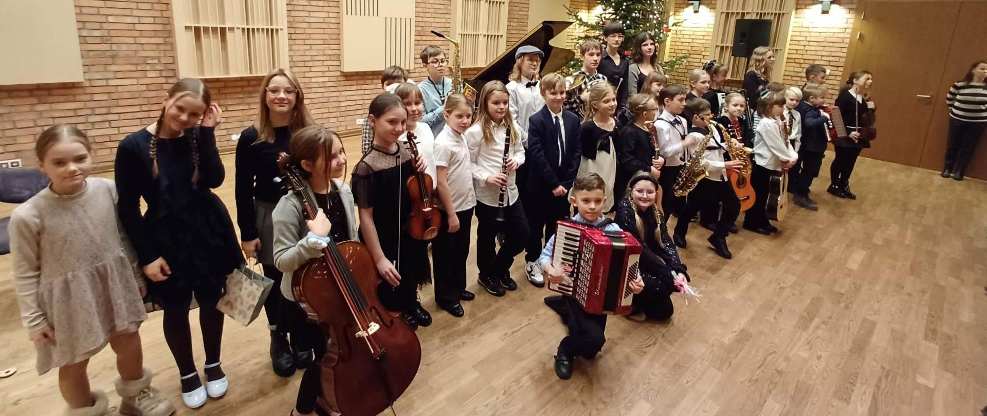 Duża grupa dzieci i młodzieży stojąca z instrumentami. W tle choinka