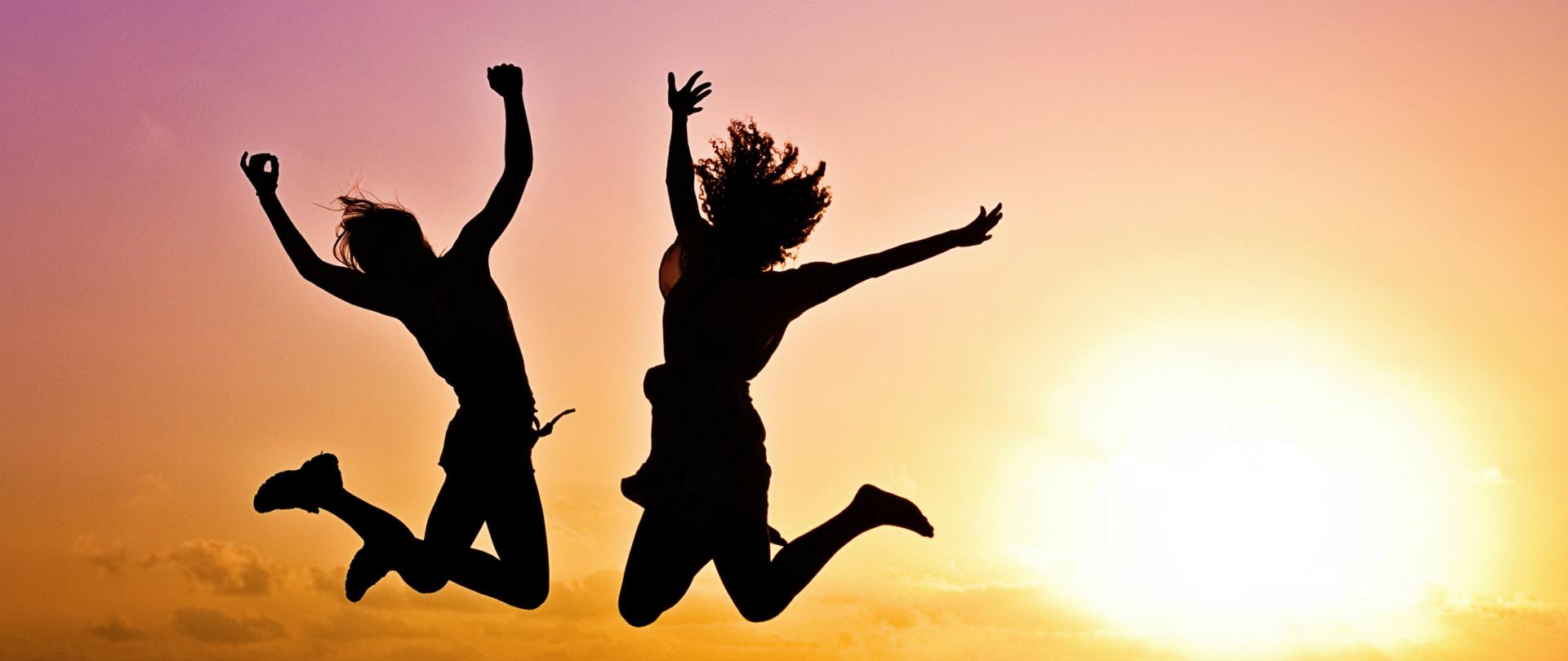 Dwoje radosnych, skaczących ludzi. W tle zachód słońca.