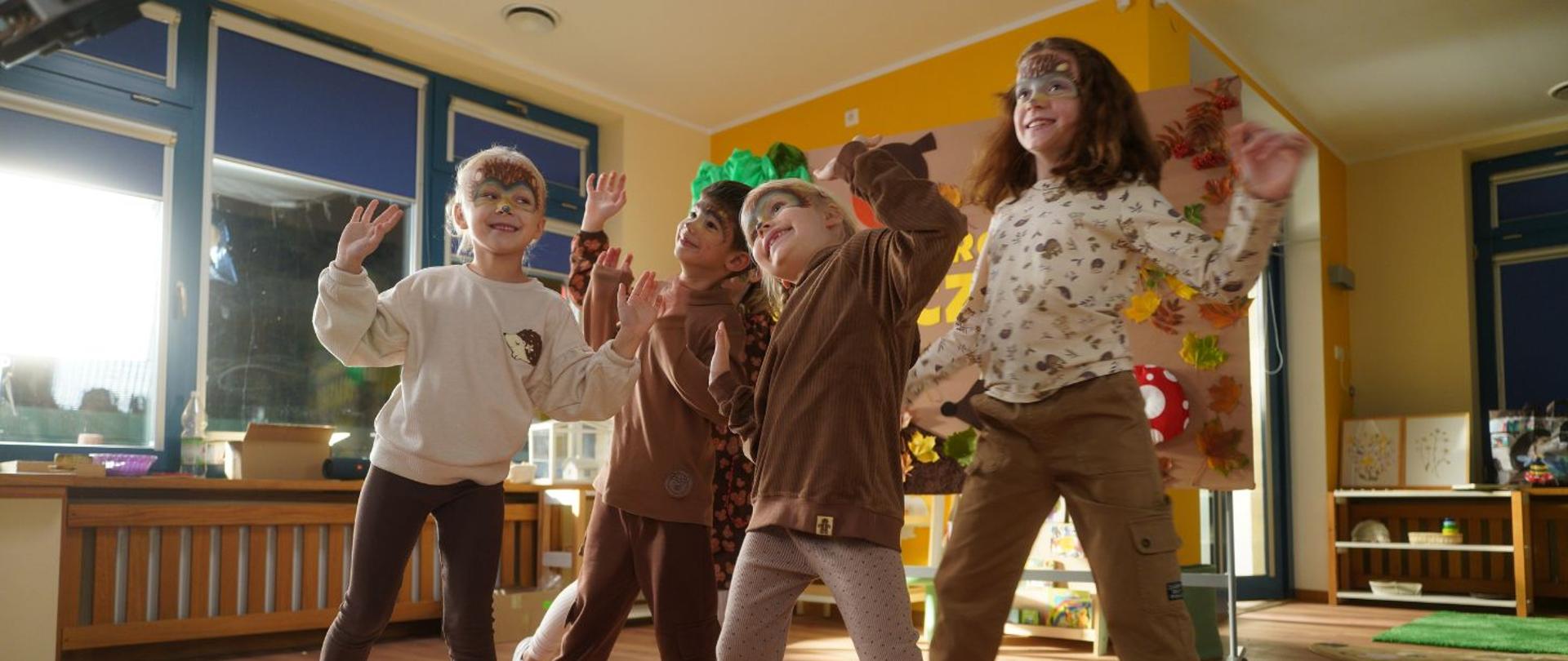 na zdjęciu widoczne są tańczące dzieci, w różnym wieku. Na twarzach dzieci namalowane są maski zwierząt. 