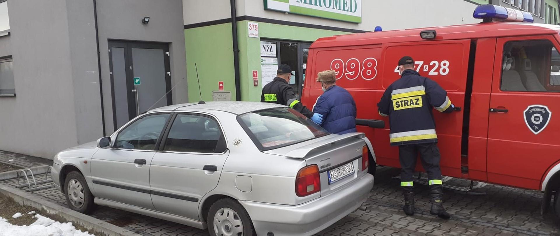 Na zdjęciu druhowie OSP pomagający dojść do placówki ośrodka zdrowia którą widać w tle.