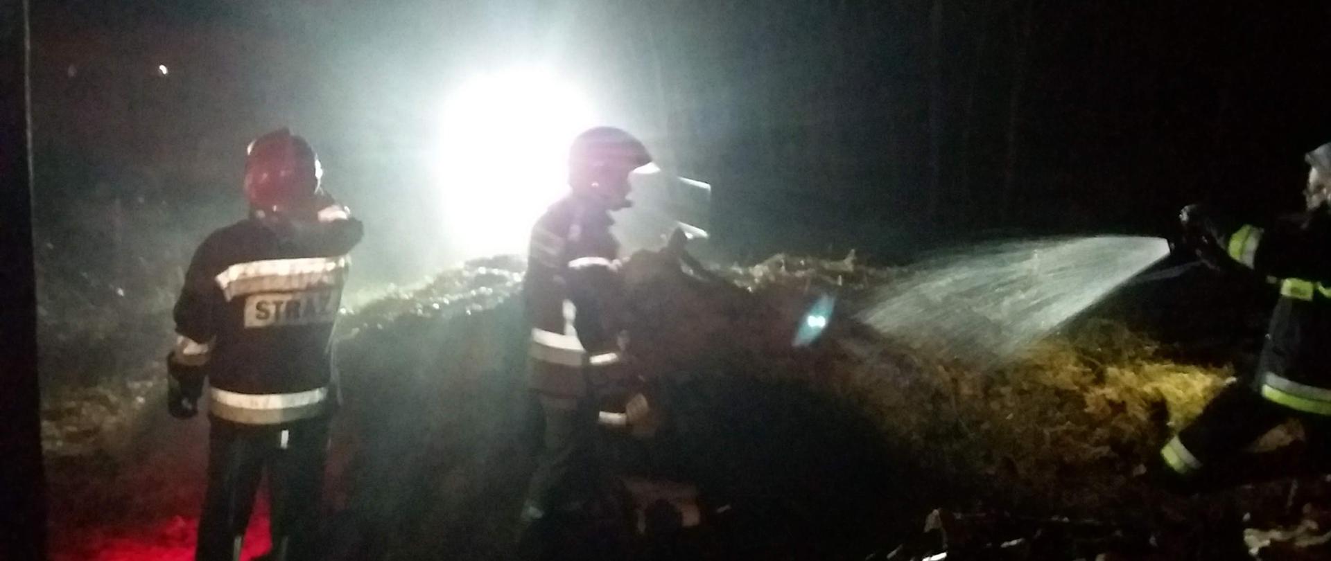Pora nocna, strażacy podczas gaszenia pożaru stodoły, w kadr zdjęcia mocno bije światło lampy