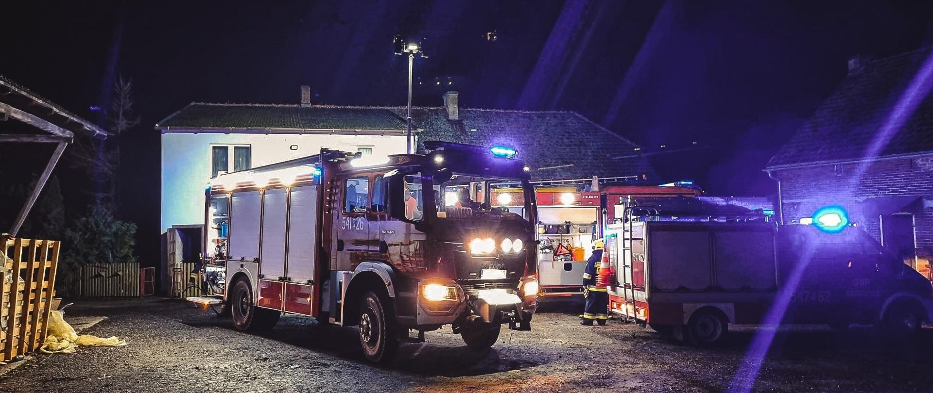 Wozy strażackie znajdują się przed obiektem, w którym doszło do pożaru. Zdjęcie wykonane w porze nocnej.
