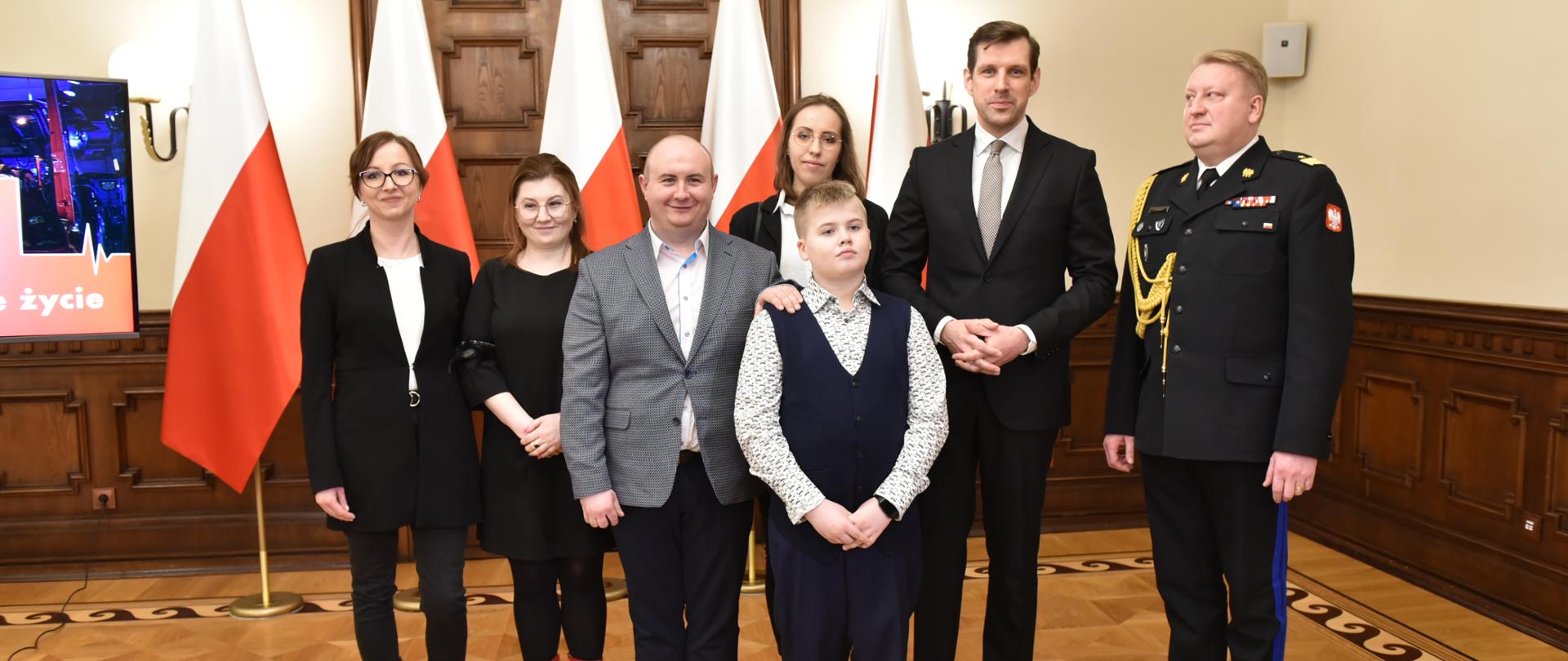 komendant wojewódzki, wojewoda łódzki chłopiec z rodzicami i dwie kobiety pozują do zdjęcia w czasie konferencji prasowej