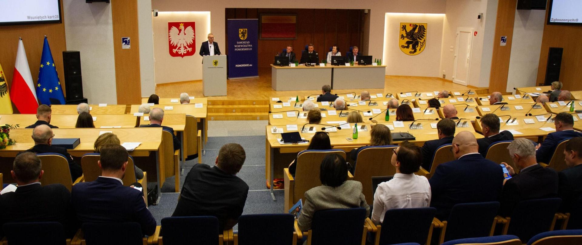 sala obrad, siedzi kilkanaście osób, ktoś przemawia, 