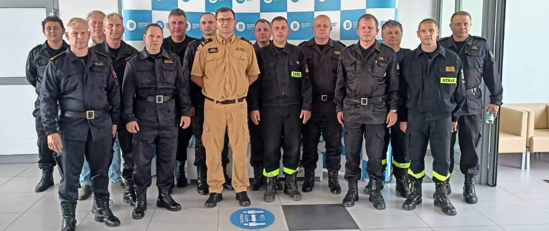 grupa strażaków stoi w holu z jasnymi podłogowymi płytkami, zdjęcie grupowe