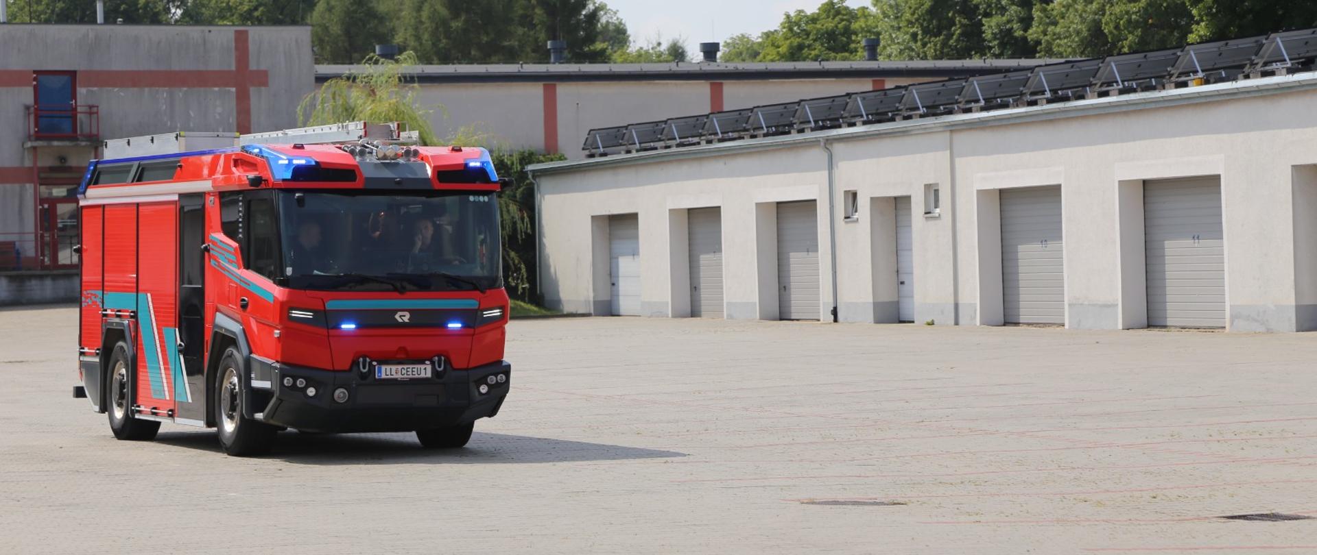 Na zdjęciu elektryczny wóz strażacki Rosenbauer RT, w głębi budynek magazynowy Centralnej Szkoły PSP

