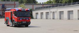 Na zdjęciu elektryczny wóz strażacki Rosenbauer RT, w głębi budynek magazynowy Centralnej Szkoły PSP