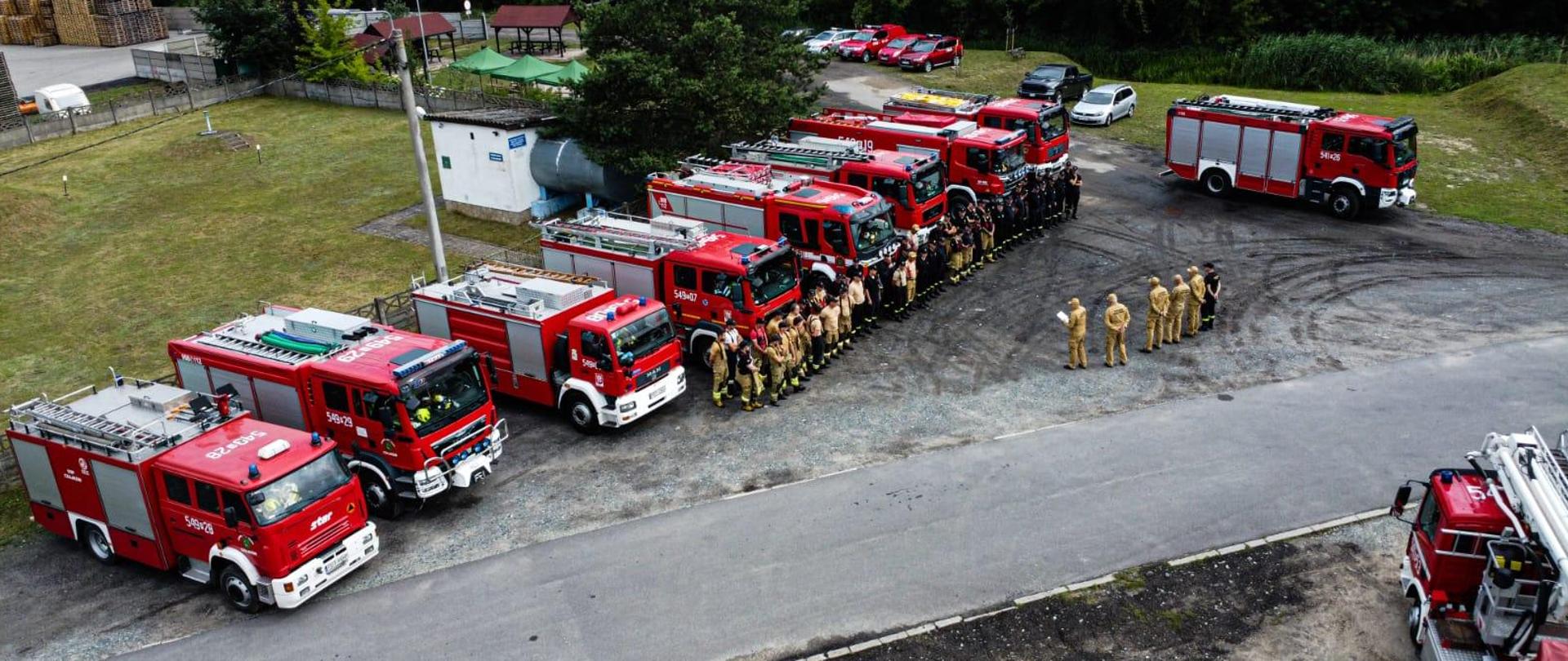 Uczestnicy wydarzenia stoją przy wozach strażackich podczas odprawy