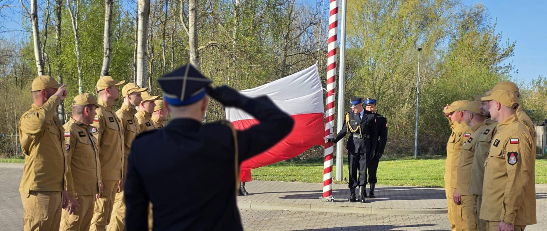 Dwie zmiany służbowe strażaków przygotowujące się do uroczystości wciągnięcia flagi na maszt.