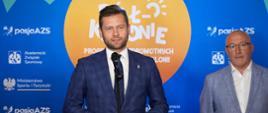 Minister Kamil Bortniczuk mówi do mikrofonu podczas briefingu. Obok stoi Dariusz Piekut, Sekretarz Generalny AZS